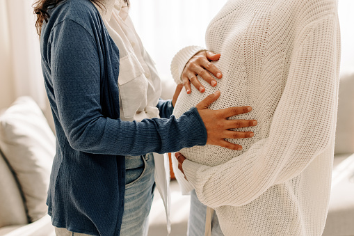 Zwei Frauen, eine davon schwanger, die andere berührt den Babybauch